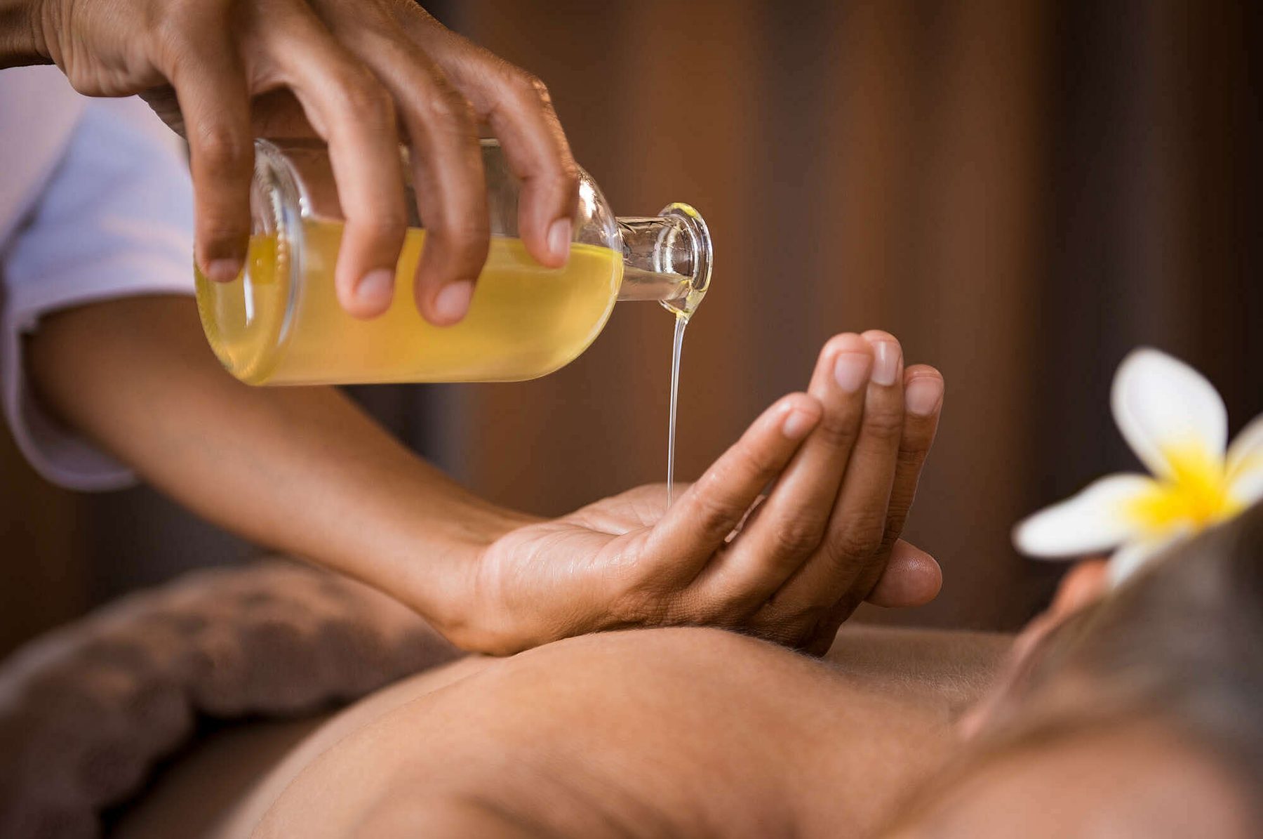 Huile de massage versée dans une main au-dessus d'un dos, lors d'un massage Édonis